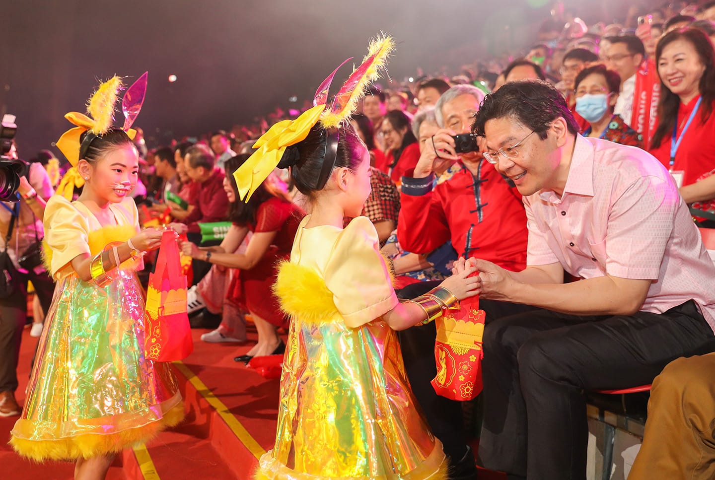 Children in yellow dresses with rabbit ear headbands greet an audience.